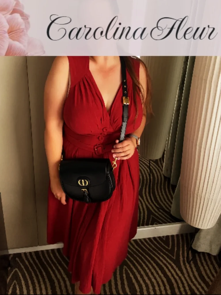 Carolina Fleur im roten Wickelkleid mit schwarzer Handtasche im Hotelflur