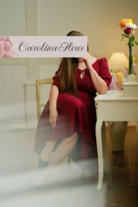 Carolina Fleur im roten Kleid an einem Schreibtisch mit Blumenstrauss