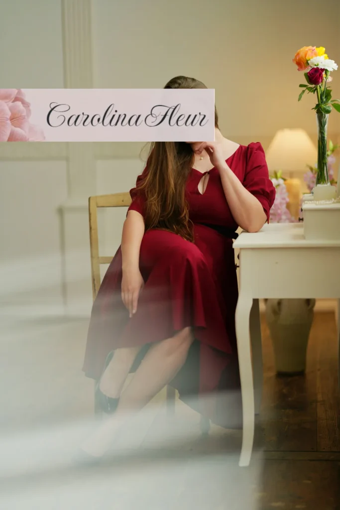 Carolina Fleur im roten Kleid an einem Schreibtisch mit Blumenstrauss