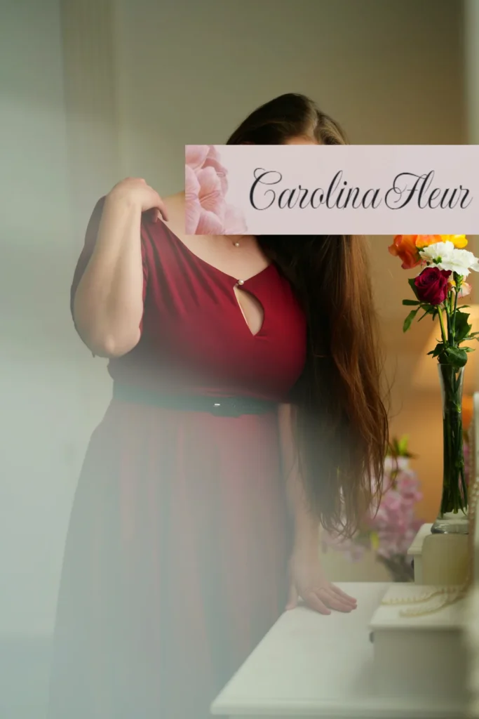 Carolina Fleur im weinroten Kleid mit Schlüssellochausschnitt neben Blumen