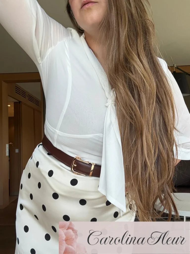 Carolina Fleur, Fly Me To You Escort und Luxury Travel Companion. In weisser Bluse, gepunktetem Rock und braunem Gürtel
