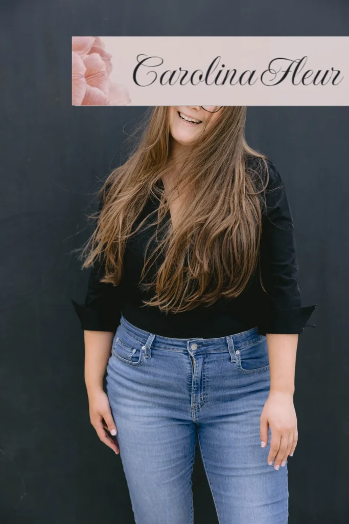 Carolina Fleur lacht in Jeans und schwarzem Oberteil vor einer dunklen Wand