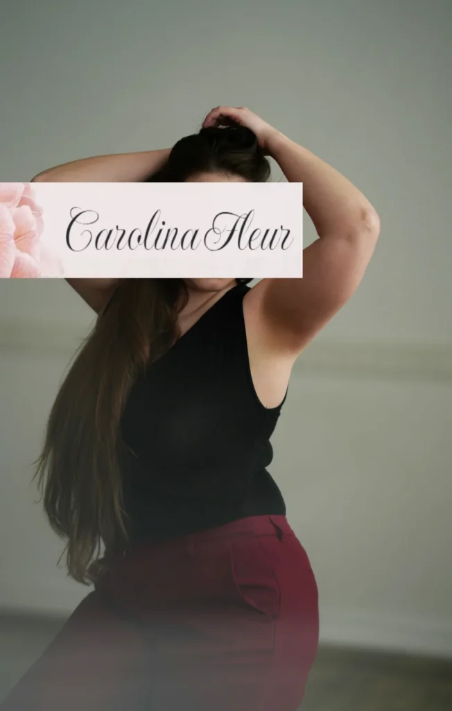 Carolina Fleur in schwarzem Top und weinroter Hose, Hände im Haar