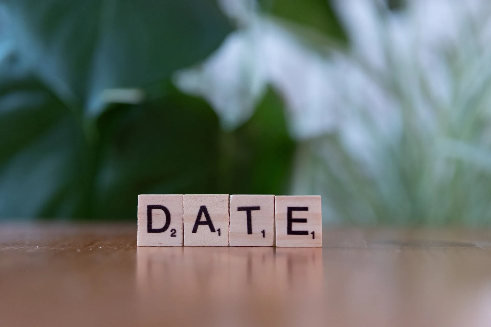 Holzbuchstaben bilden das Wort „Date“ auf einem Holztisch vor unscharfem grünem Hintergrund